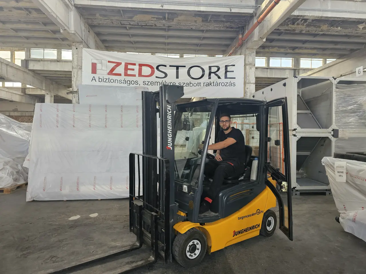 ZedStore munkatárs targoncával a fóliázott, letakart raktári tételek között